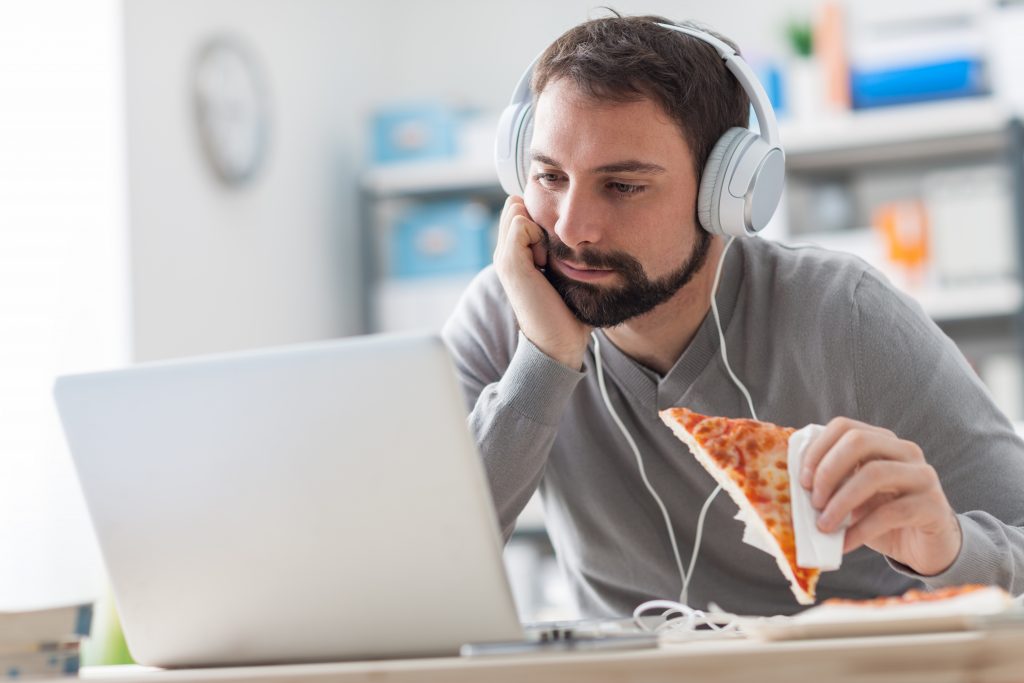 A man eating pizza by a laptop