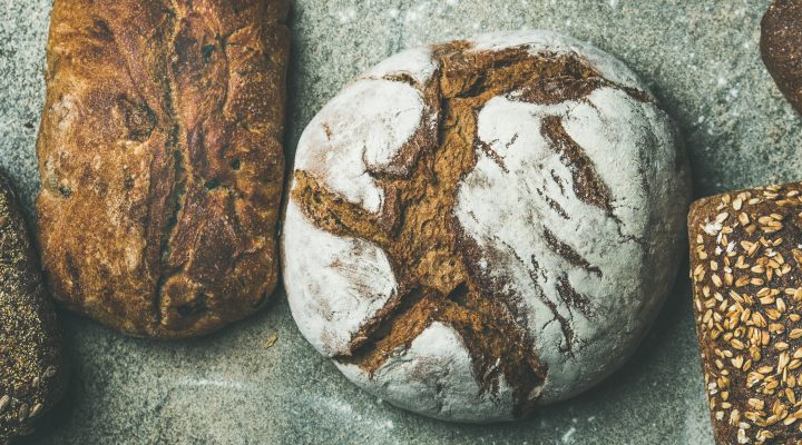 Various bread selection flat-lay. Top view of Rye, wheat and multigrain rustic bread loaves over grey concrete background, wide composition