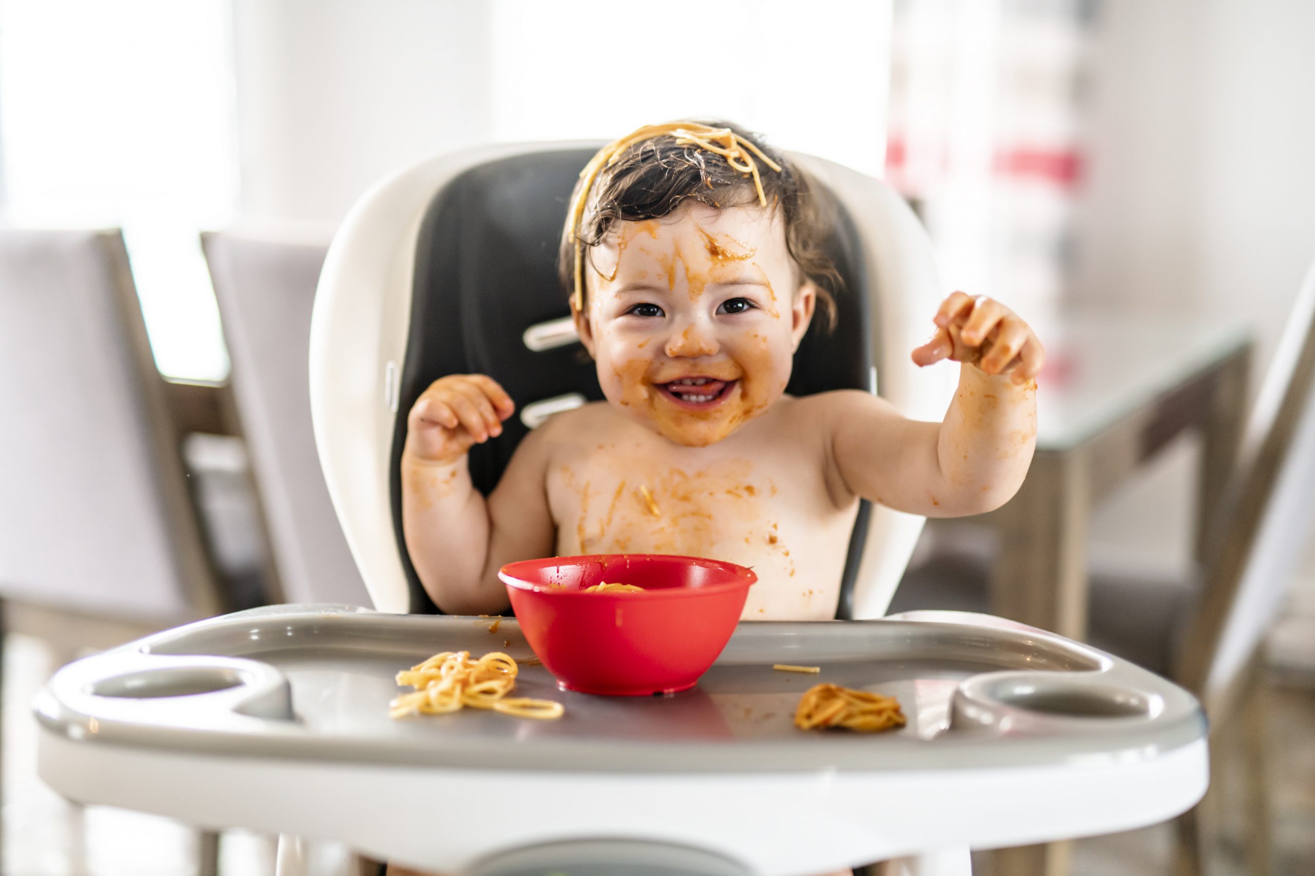 toddler in a high chair eating spaghetti