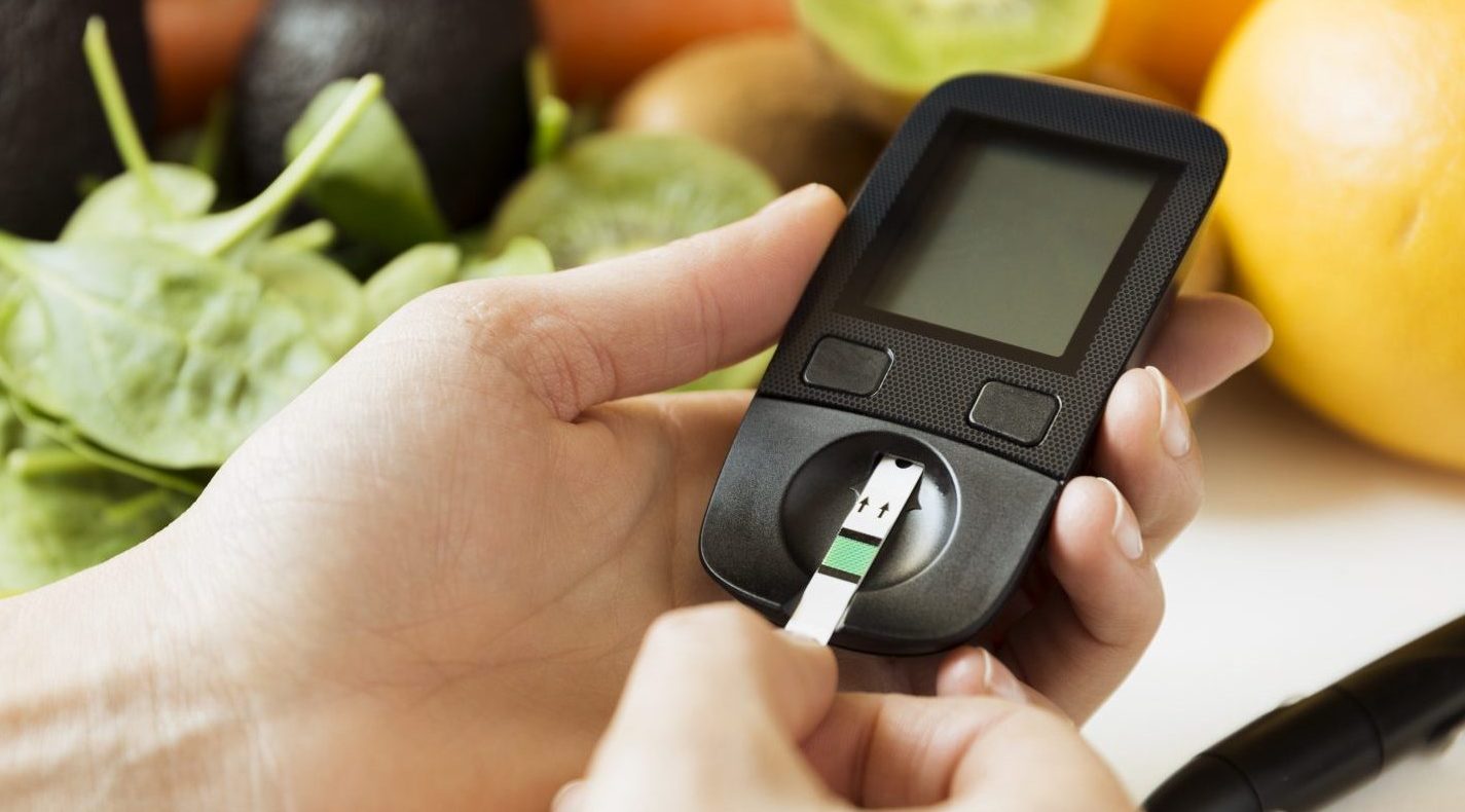 Diabetes monitor in a persons hand, healthy foods