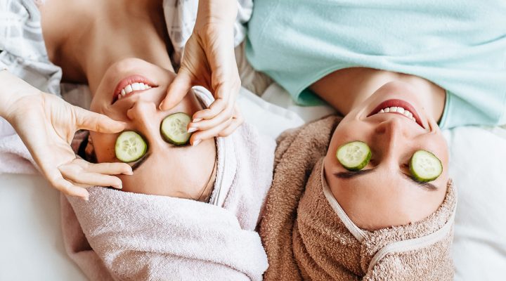 Two girls make homemade face and hair beauty masks. Cucumbers around the eyes.