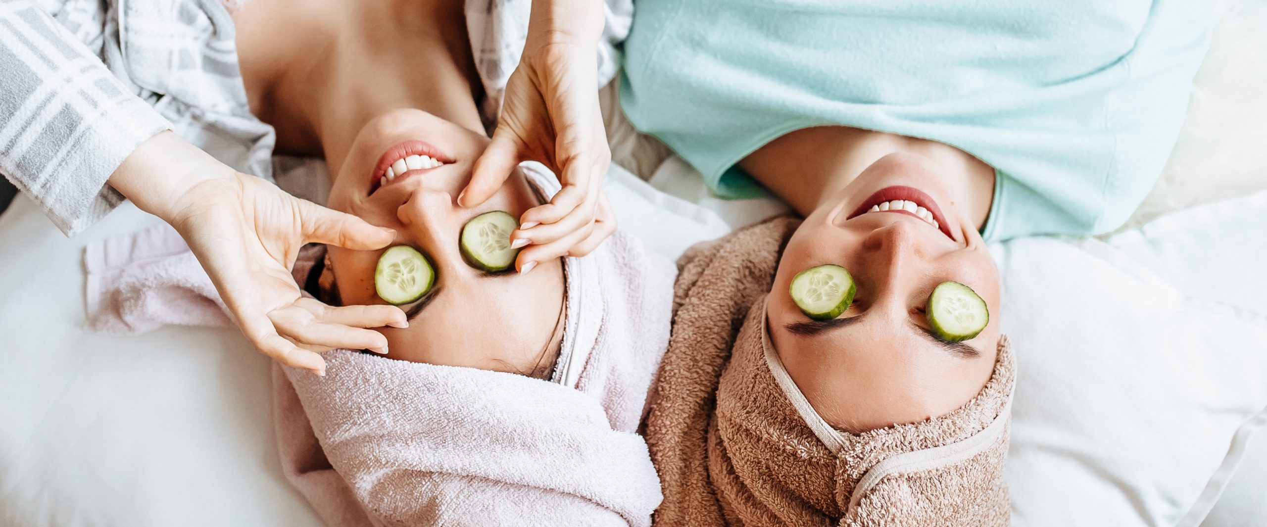 Two girls make homemade face and hair beauty masks. Cucumbers around the eyes.