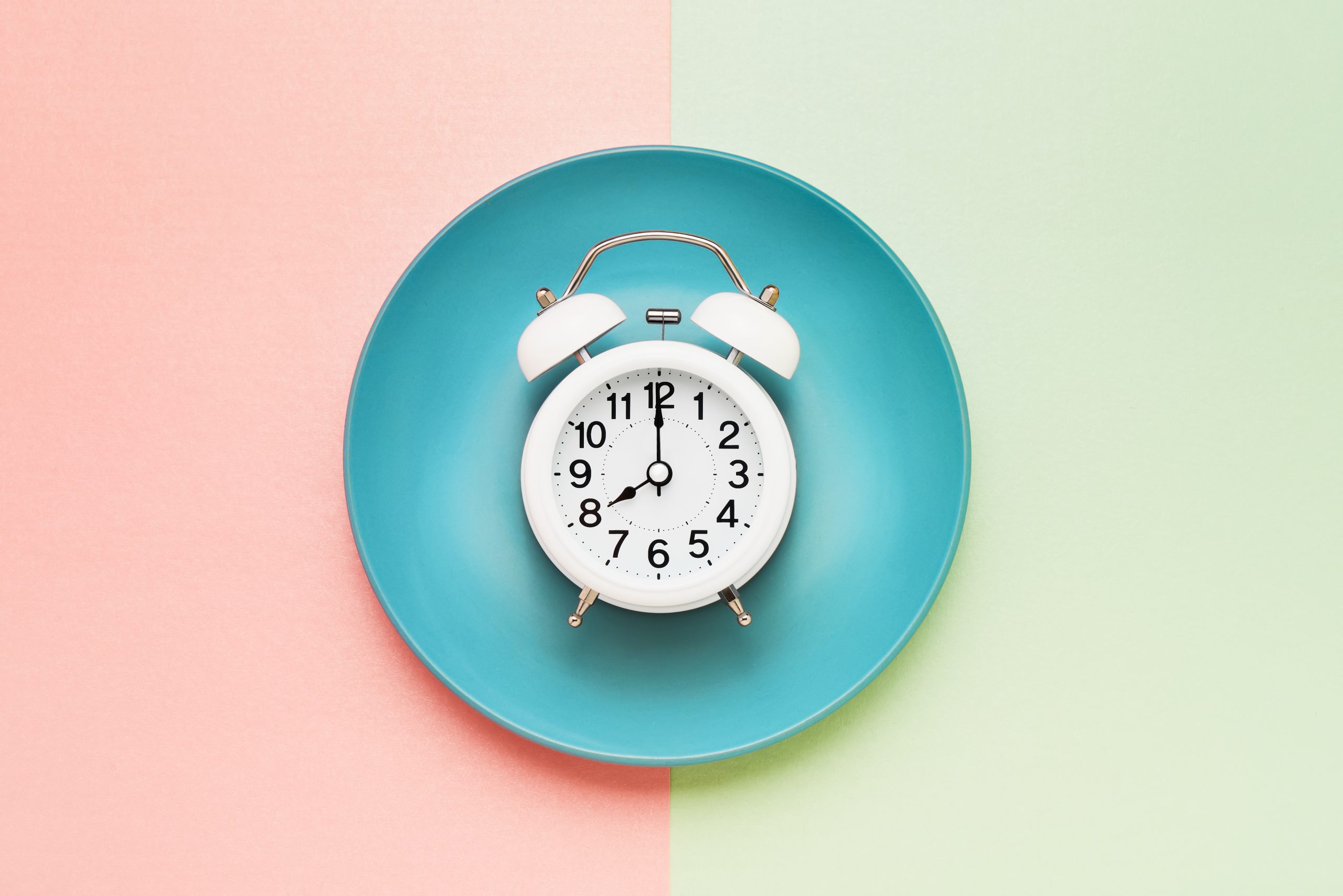 Intermittent fasting concept. White alarm clock on empty blue plate. Top view, copy space