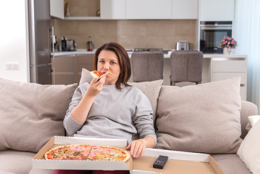A person eating pizza alone on the sofa