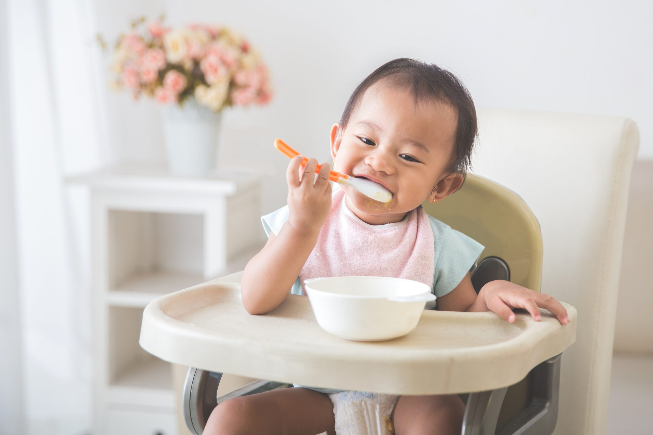 baby girl sitting on high chair and feed her self