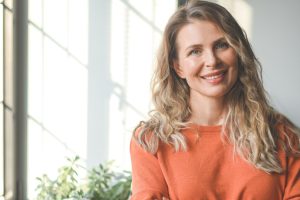 A light haired woman, wearing a peach colour sweater